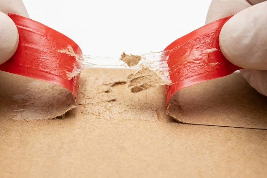 Zbliżenie dłoni odklejających czerwony pasek kleju z tekturowej koperty kurierskiej